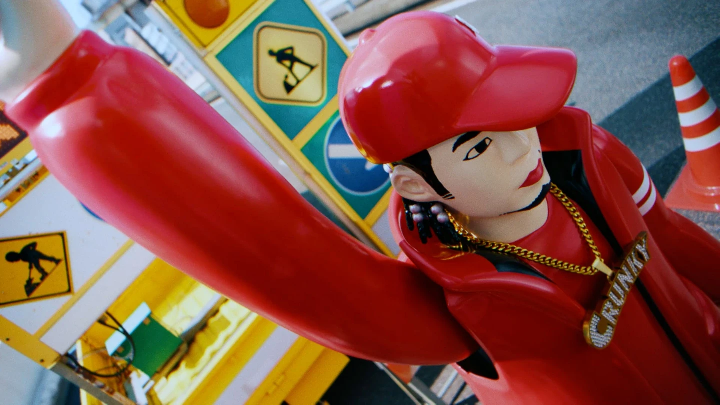 赤い帽子とネックレスを着けたDiggy-MO’風ロボットが、工事の標識やコーンと並ぶCMの場面。