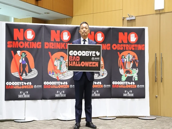 渋谷区の会見写真。区長の前にGOODBYE BAD HALLOWEENのポスター、背後に路上飲酒などのNO表示が並ぶ。