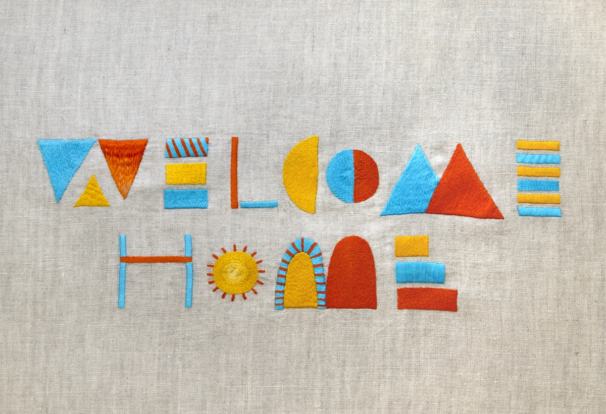 Maricor/MaricarのWest Elm向けWelcome Home。リネン上に、文字を幾何学模様のように組み合わせた色鮮やかな刺繍。